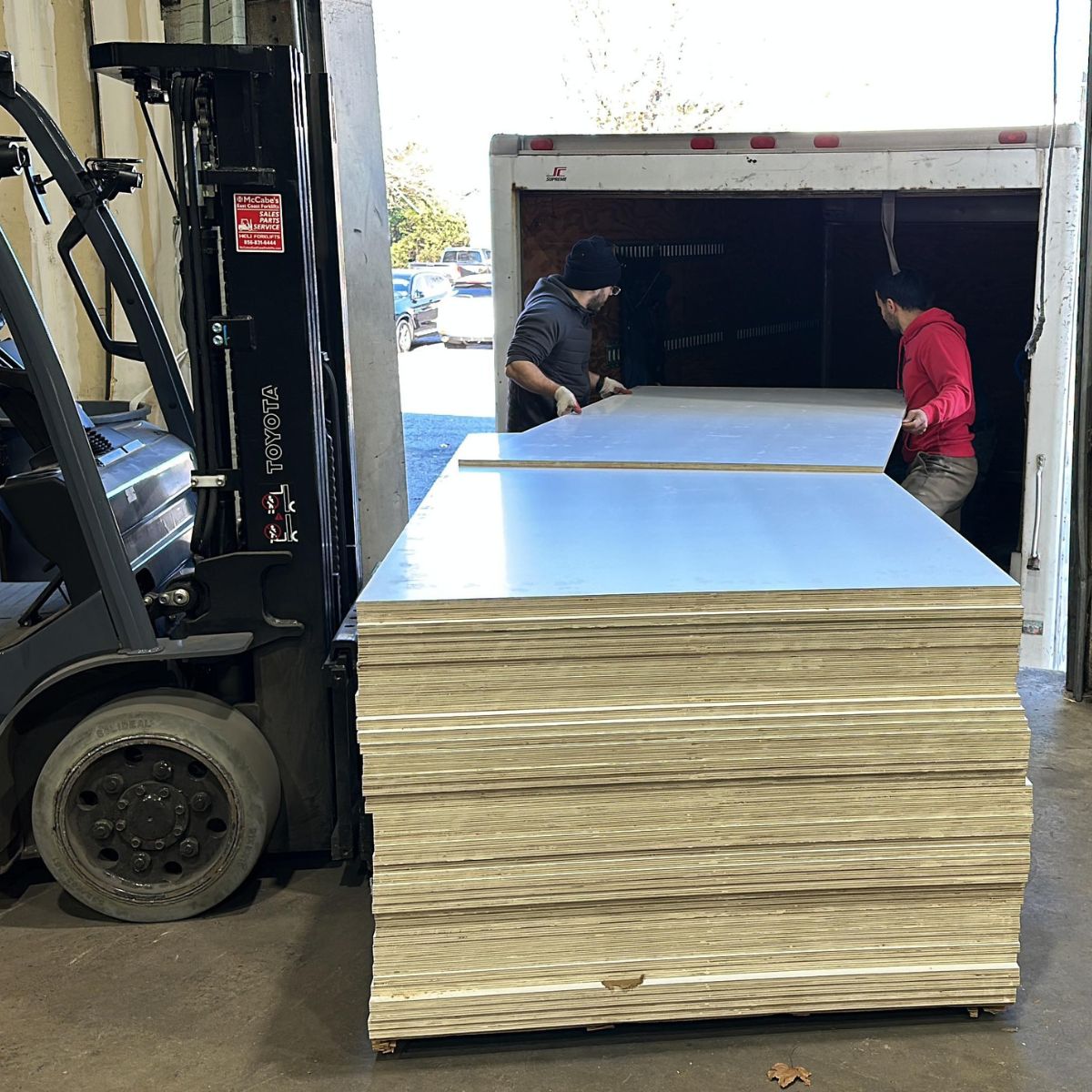 Forklift unloading cabinet-grade plywood sheets from delivery truck in New Jersey